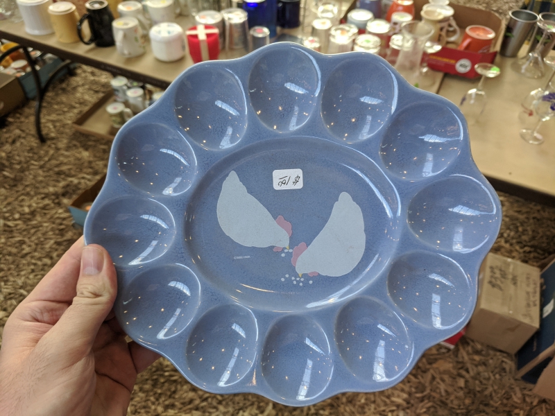 A blue dish that has holders for deviled eggs, and two chickens painted in the center.