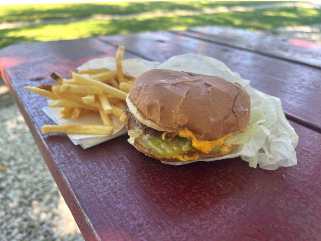 On a red picnic table, there is a cheeseburger from Just Hamburgers in Paxton, Illinois with a side of fries. Photo by Alyssa Buckley.