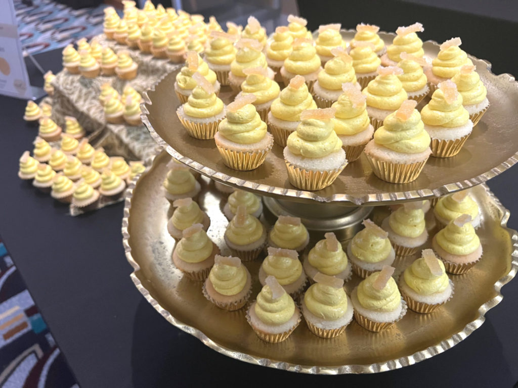 On a black table, there is a gold tiered cupcake stand with miniature lemonade cupcakes. Photo by Alyssa Buckley.