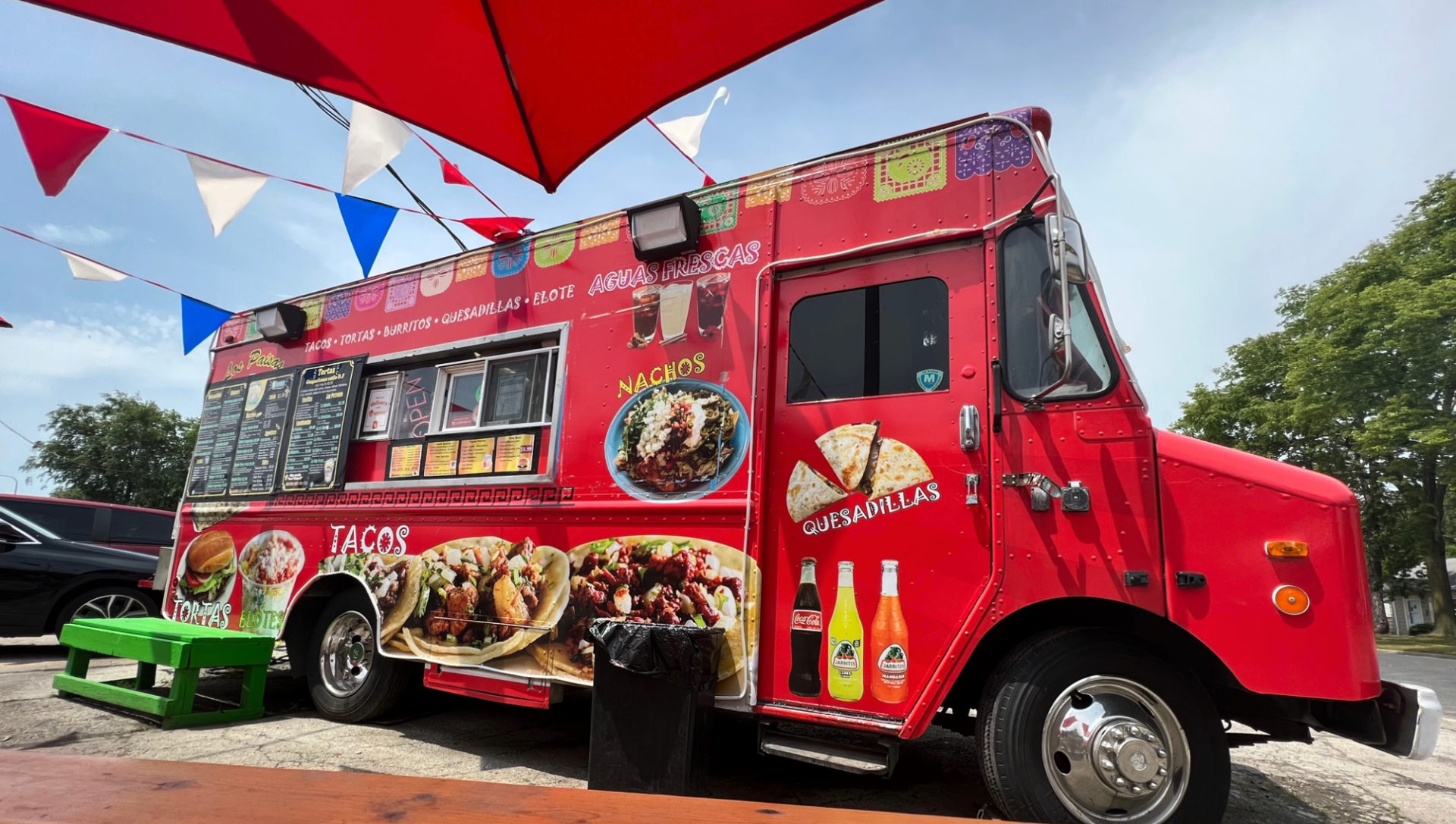The red truck for Los Paisas food truck on Cunningham Avenue in Champaign. The truck has a black menu on the outside in addition to red, white, and blue pendant flags on banners connected to the umbrella tables. Photo by Alyssa Buckley.