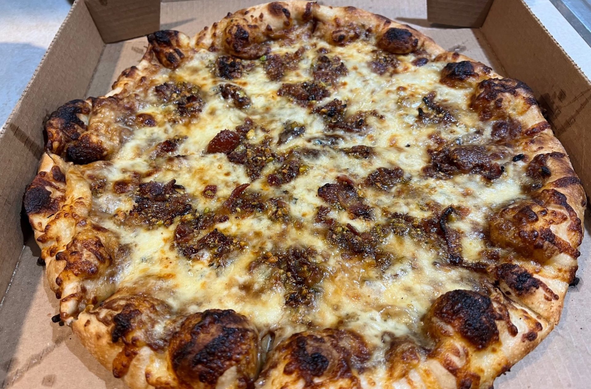 A round apple butter bacon pizza in a cardboard takeout box.
