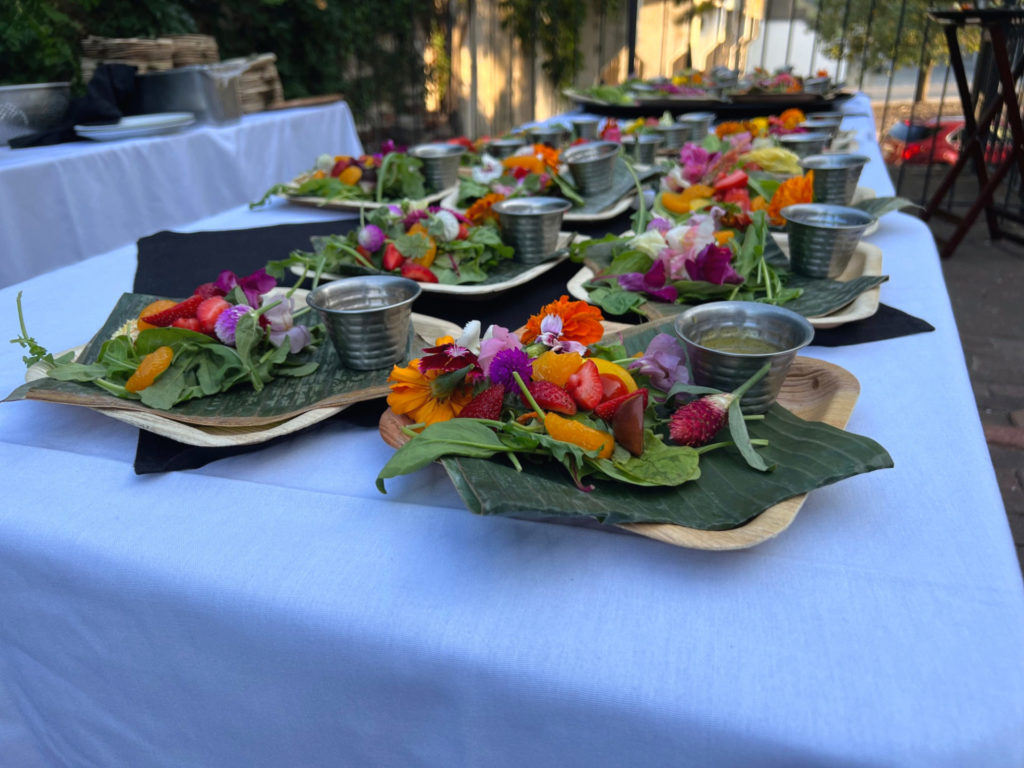 A white table has many prepared colorful summer salads with edible flowers and small silver cups of tequila vinaigrette. Photo by Alyssa Buckley.