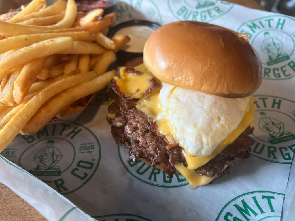 On a tray, there is a burger with an overeasy egg, American cheese, and bacon by Smith Burger Co. Photo by Alyssa Buckley.