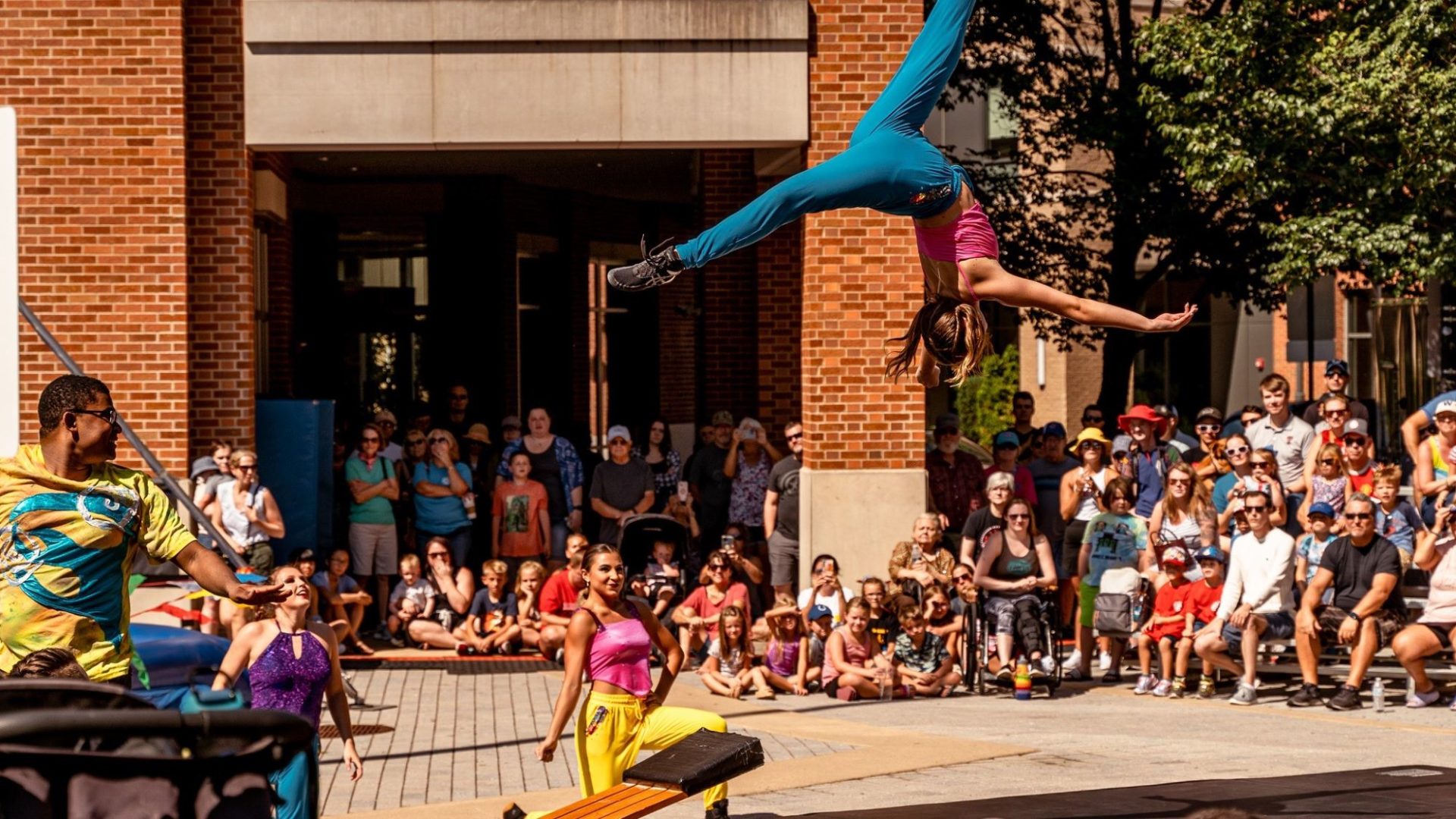 A circus peformer is mid-flip, high in the air, while a crowd looks on.