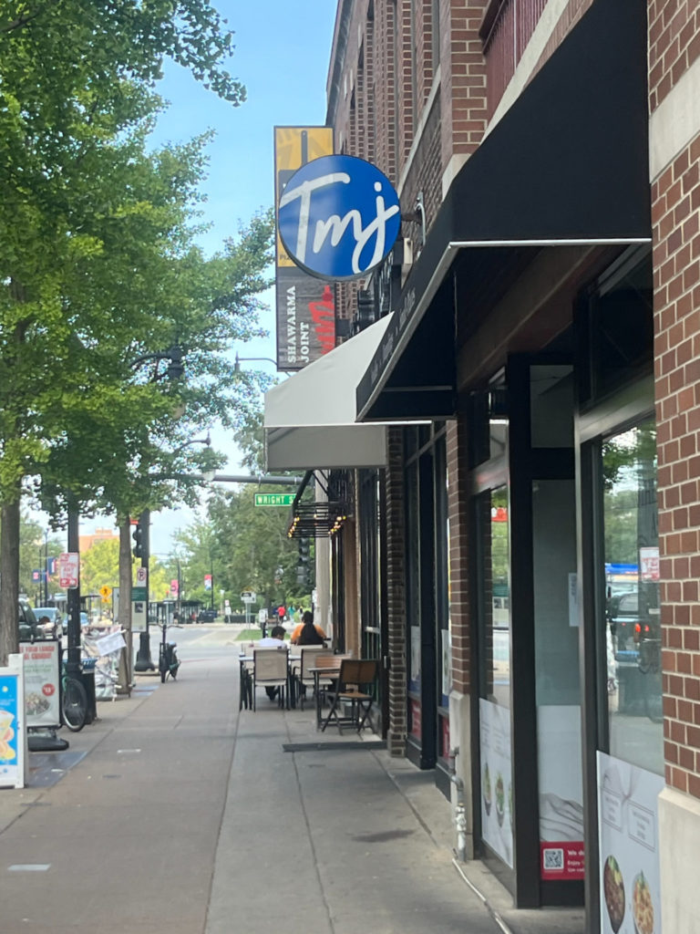 Outside of Teamoji in Campustown, there is a round blue sign with Tmj in white. Photo by Ayesha Mehta.