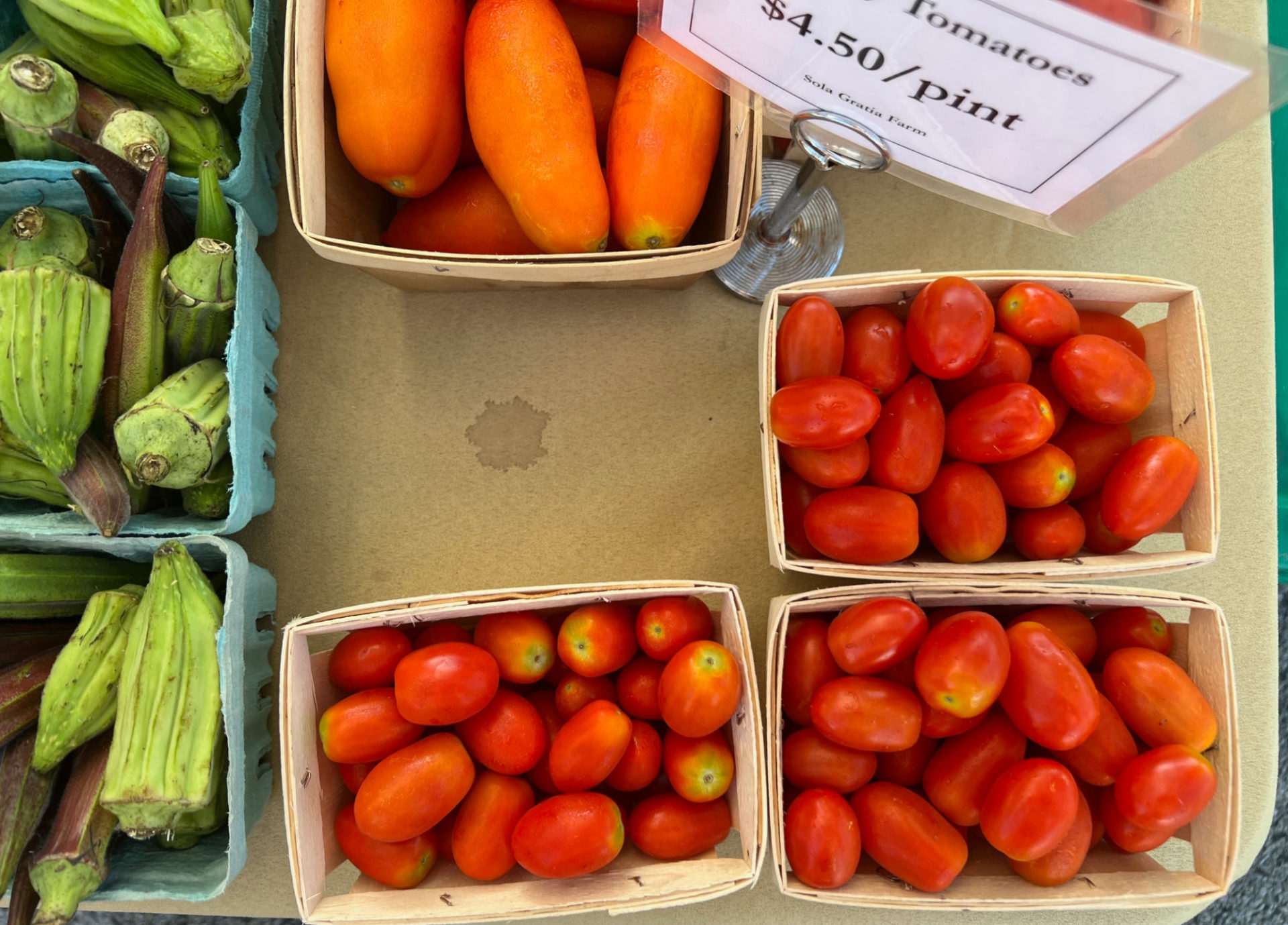 An overhead photo of tomatoes, okra, and mini peppers for sale at the Urbana farmers' market. Photo by Alyssa Buckley.