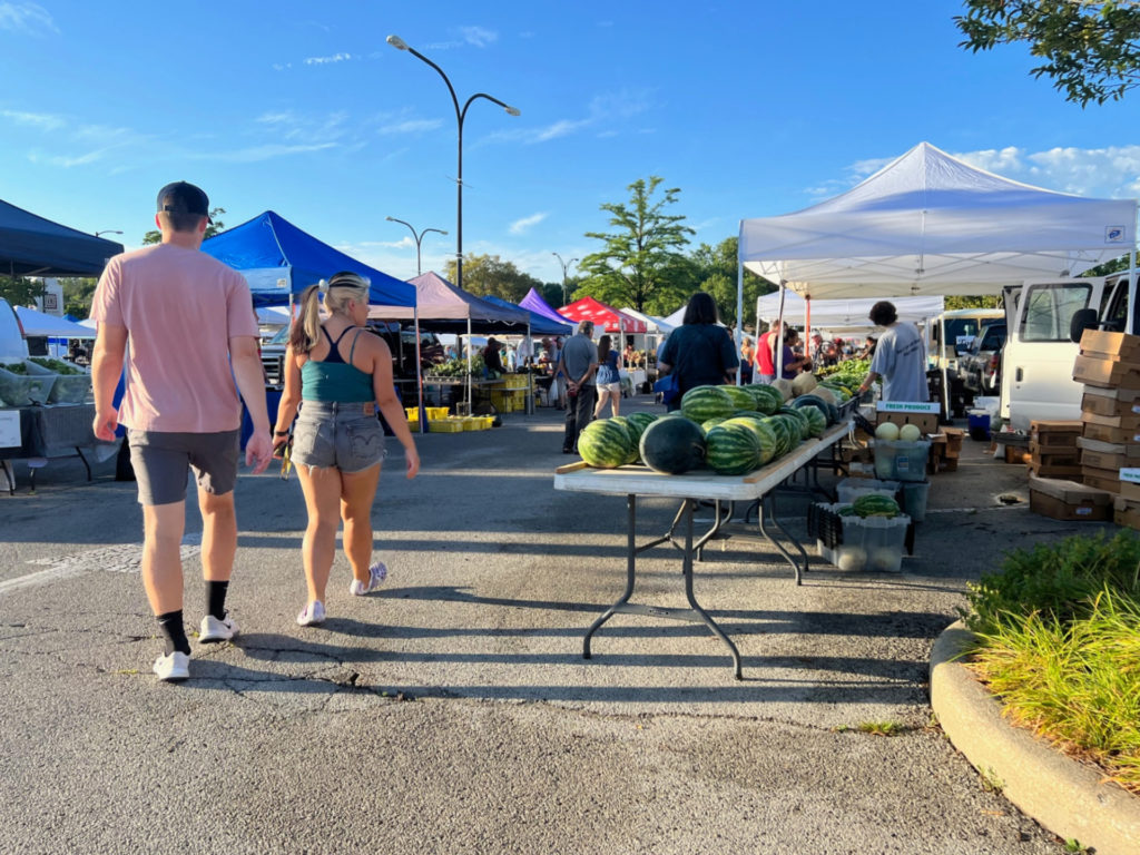 Two people in shorts walk into the Urbana Market at the Square on a Saturday morning with bright blue skies. Photo by Alyssa Buckley.