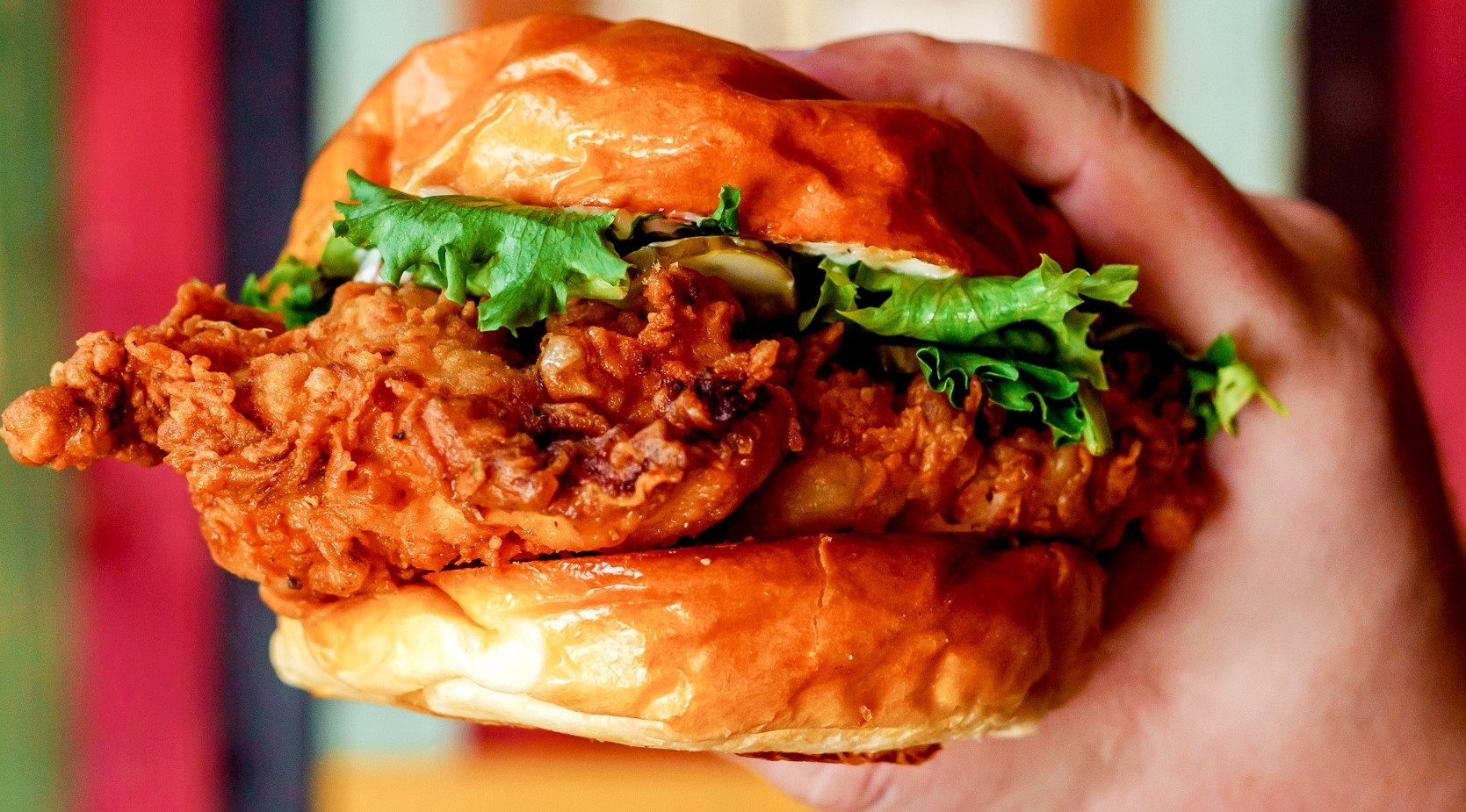 A hand holding a large breaded chicken sandwich with lettuce.