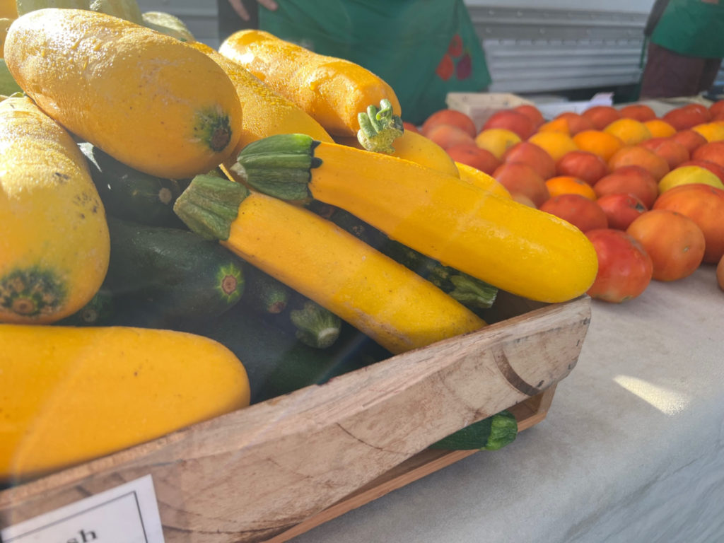 Yellow squash and zucchini are in a wooden basket on a table for sale at the Urbana farmers' market. Photo by Alyssa Buckley.