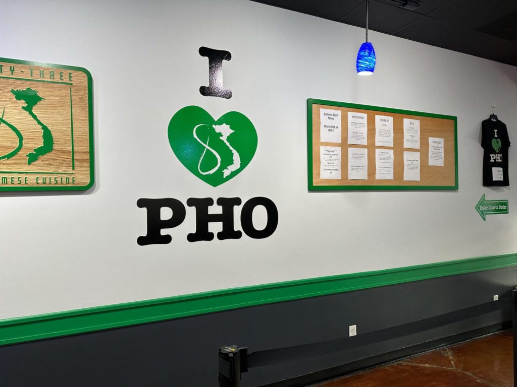 Inside 83 Vietnamese, there is a sign reading "I (green heart with the outline of Vietnam in white) PHO" on a white wall.