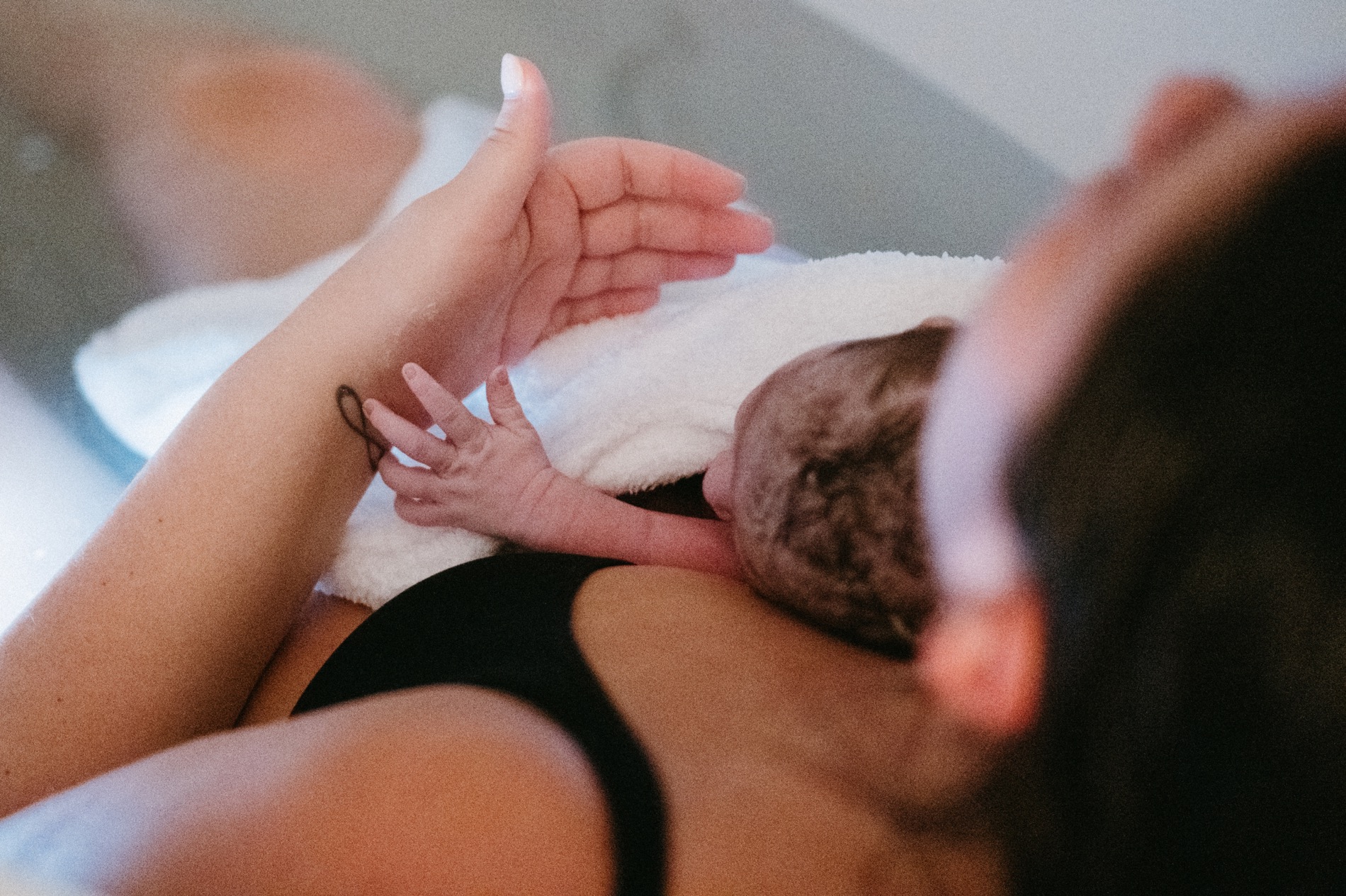 A mother and a newborn baby in a tub, hands touching