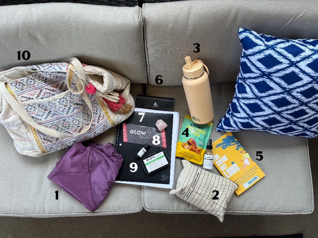 A close up shot of a white couch. On it are items from Lola's bag each item has a number next to it. Some of them include a purple folded yoga tank top, a white bag with a faded design embroidered, a peach water bottle and a book with a yellow cover. 