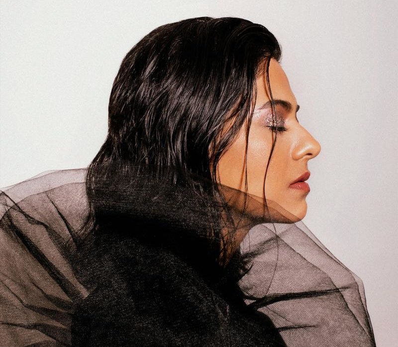 Arushi Jain in side profile. Her eyes are closed while facing to the right. She is a young Indian woman, with long dark hair which is hanging loose. She has purple eyeshadw and red lipstick. She is wearing a black outfit with an exaggerated tulle circular sleeve that takes up the entire bottom half of the photo and obscures her chin.