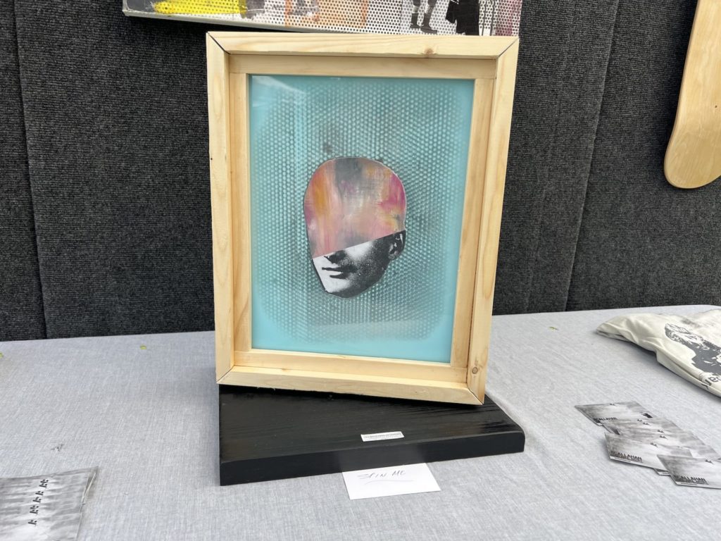 Double sided painting stands vertically on a black stand on a table. Gold frame with turquoise background; there is a man's face in the center, but only the bottom half of the face is drawn