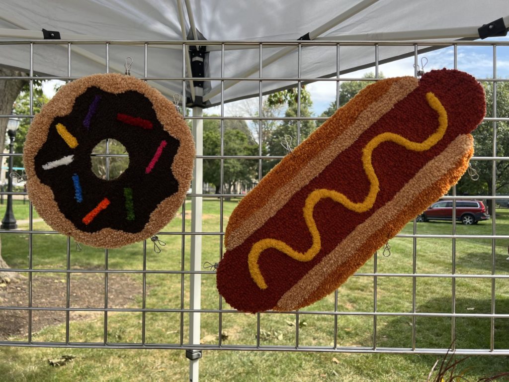 two rugs are displayed on a metal vertical display: left is a donut, right is a hot dog