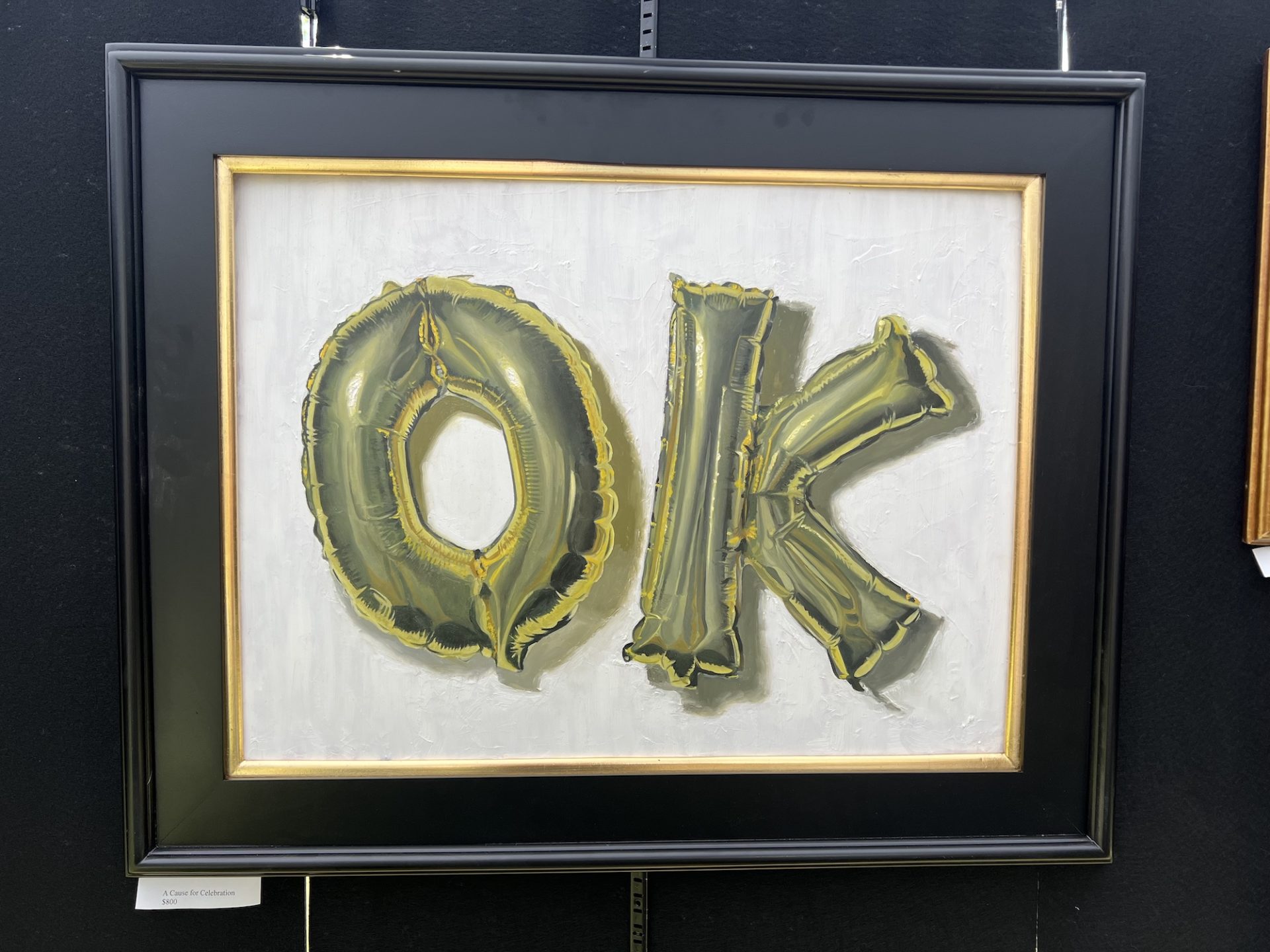 realist painting of gold letter balloons spelling "OK" in a black frame