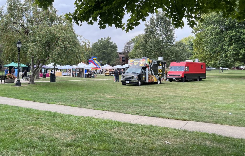 Food trucks are lined up in the grass with the art fair visible in the back
