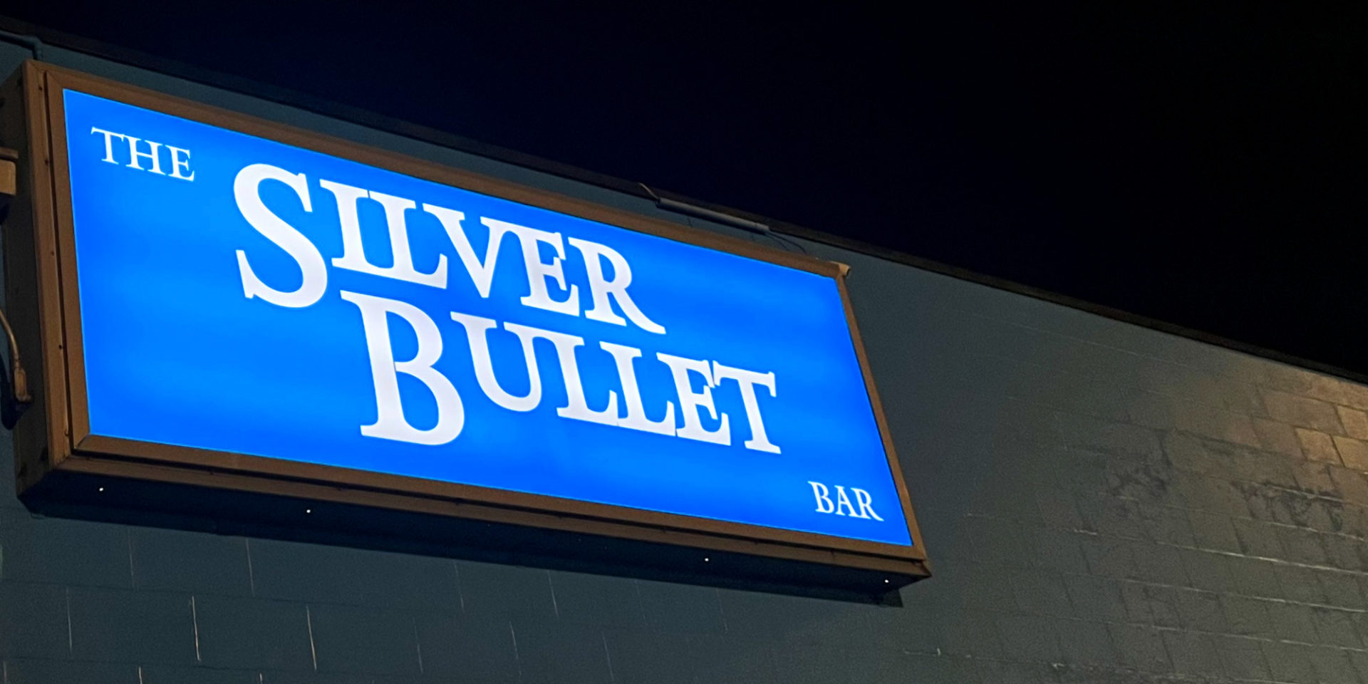 The Silver Bullet Bar at night with the blue sign illuminated.