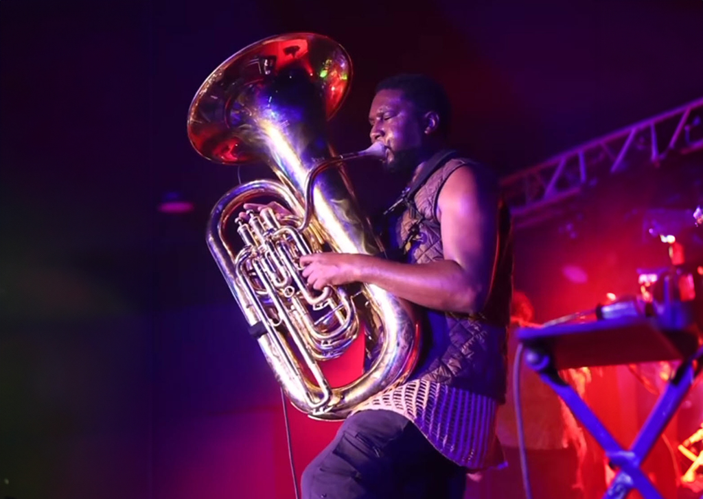 A black man up on a stage playing a tuba under dim red lights