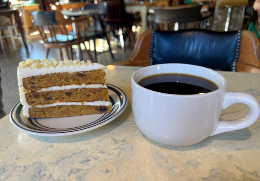 At Caffe Paradiso, a slice of carrot cake on a real plate and a giant mug of coffee are on a marble table.