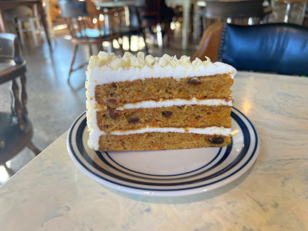 A large slice of carrot cake with white frosting and curls of white chocolate.