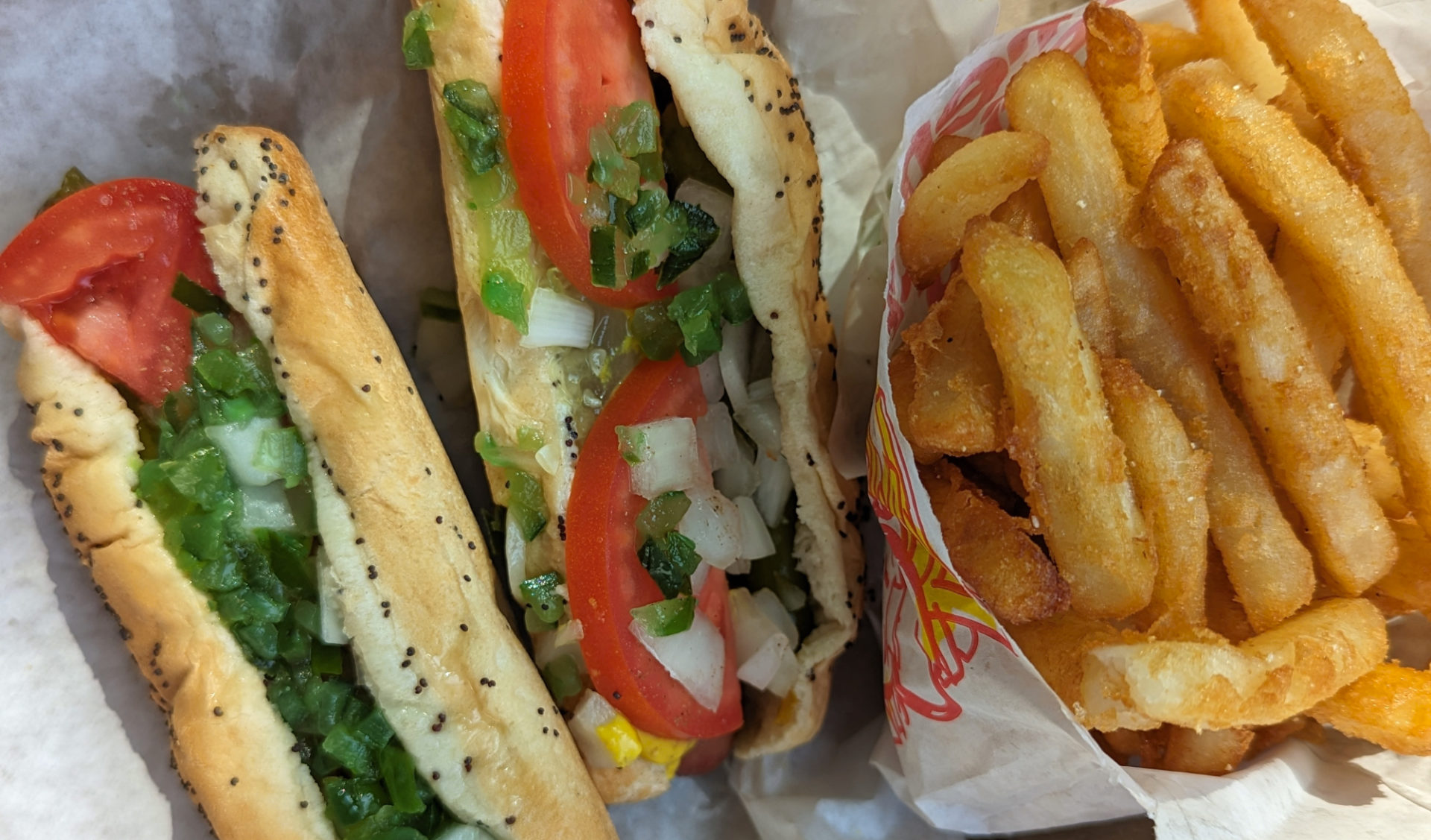 A cropped photo of two Chicago dogs from Windy City with a side of fries.
