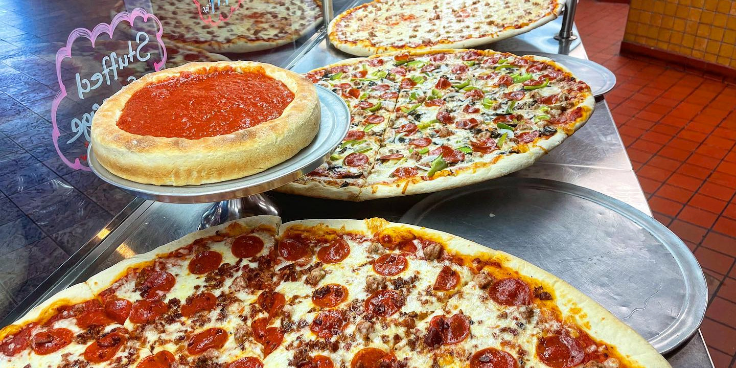 Chicago pizzas at Bacci Pizzeria in Chicago. The pieces are full, no slices have been removed. One small deep dish is raised above jumbo pizzas.