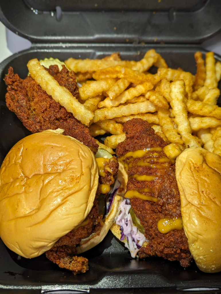 An order of sandwiches from Dave's Hot Chicken in Champaign, Illinois in a black styrofoam container.
