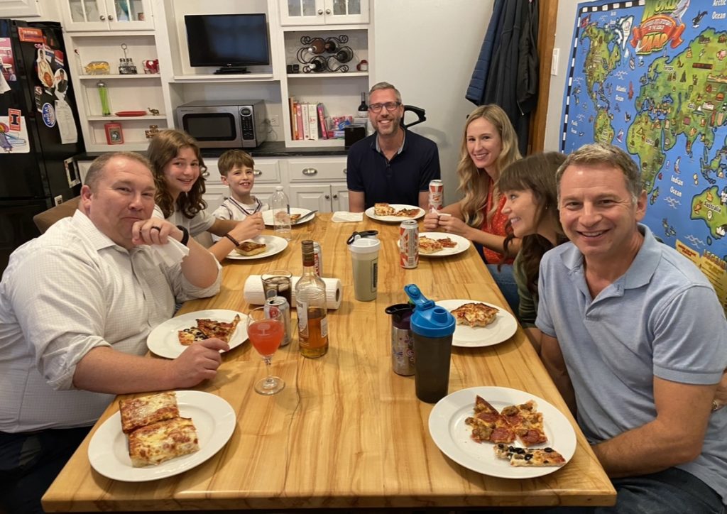 Senator Faraci is gathered around a table with Senator Bennett, Mike Frerichs, and some of their families. They are eating pizza.