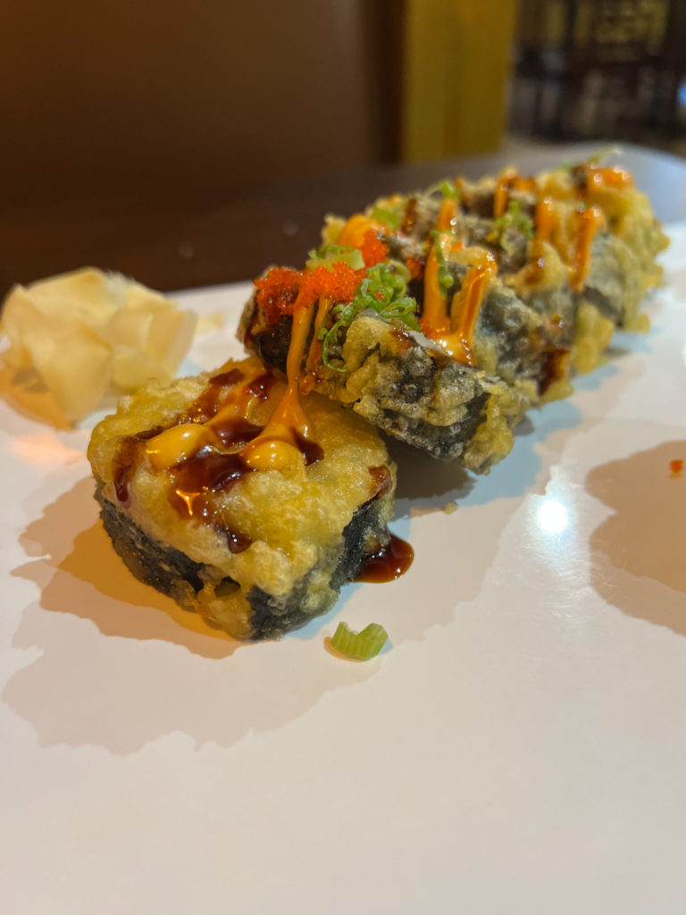 A deep fried sushi roll with orange and eel sauces.