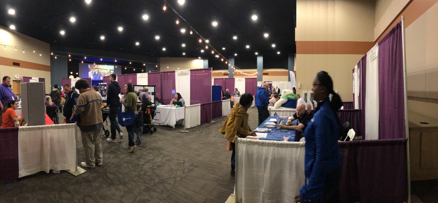 An expo being held in a large event space. There are resource tables and people milling around and visiting the tables.