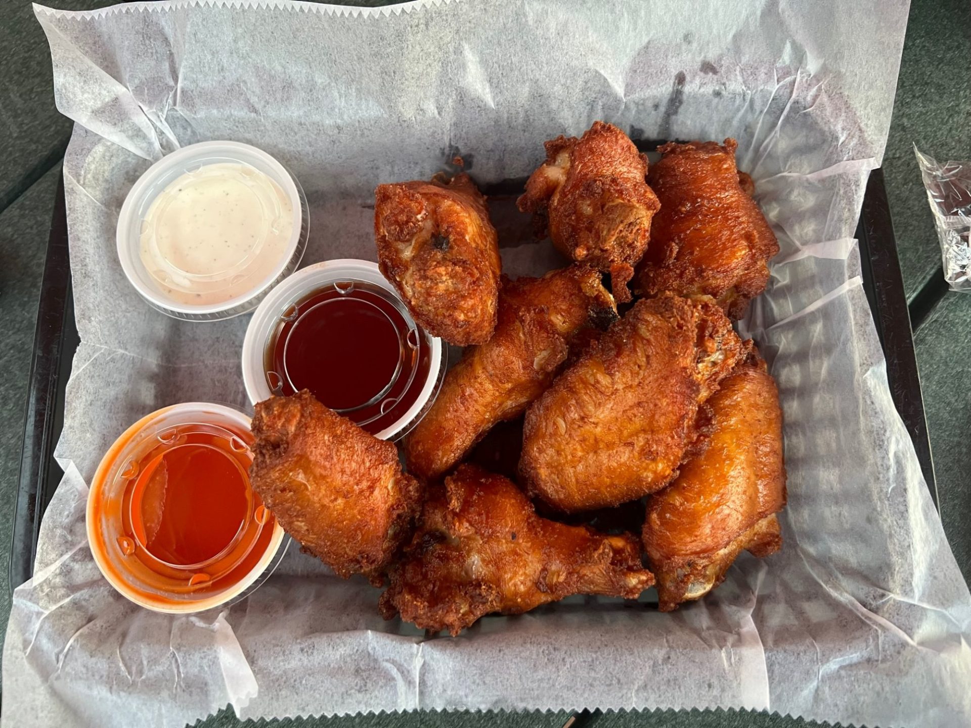 A basket lined with wax paper, with eight wings piled on one side, and three dipping sauces on the other.