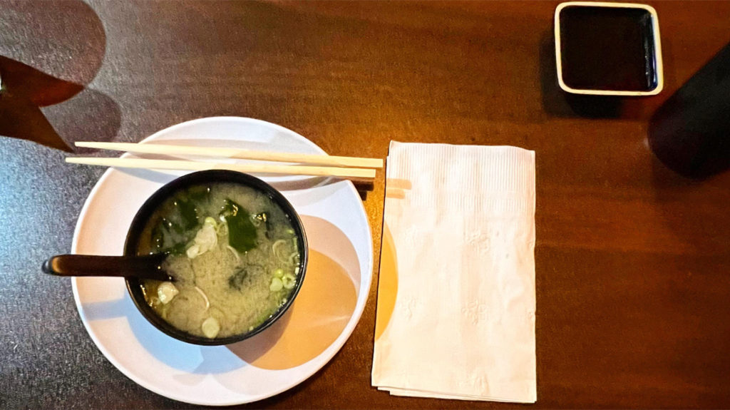 A bowl of miso soup with wooden chopsticks and a white paper napkin.