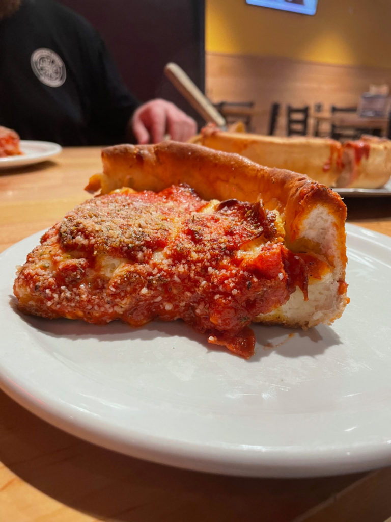 A single slice of deep dish pizza at Papa Del's in Champaign with red sauce sits on a white plate.