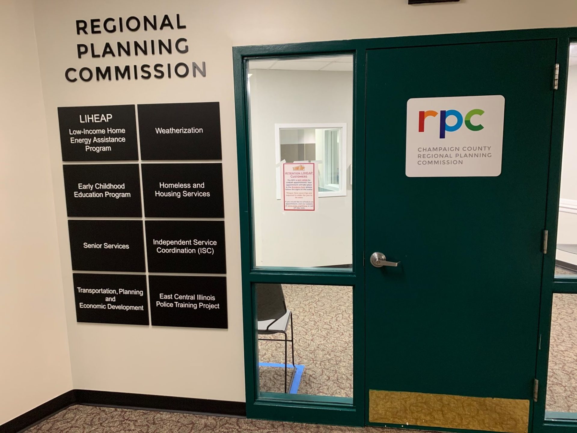 The entrance to the regional planning commission office. It has a black door with windows alongside it, and signs indicated provided services on the wall beside it.