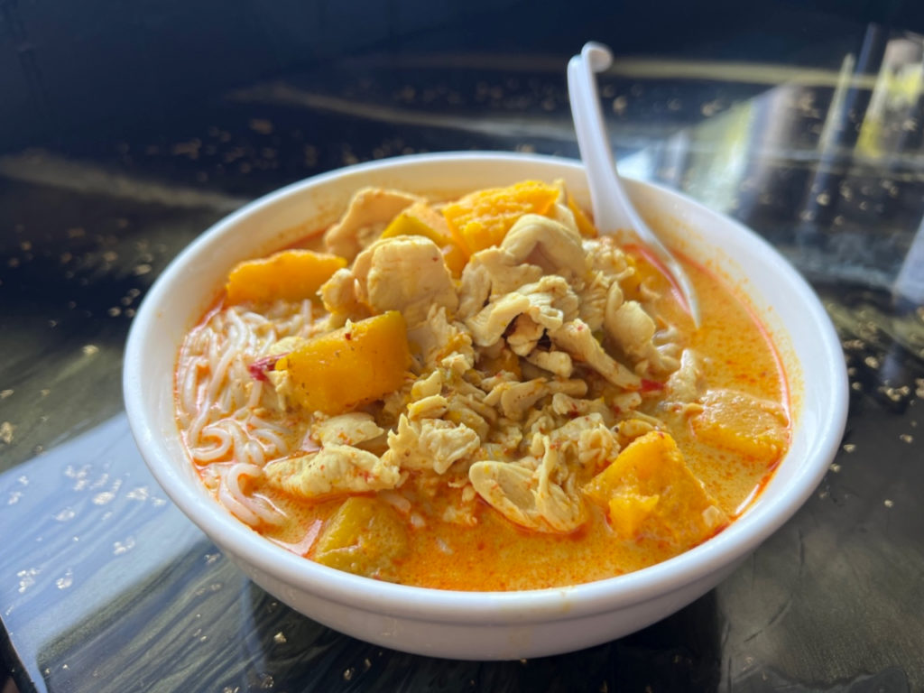 At Sticky Rice in Champaign, Illinois, there is a white bowl of pumpkin curry with chicken added.