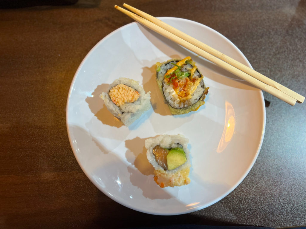 Three pieces of sushi on a white plate with wooden chopsticks.