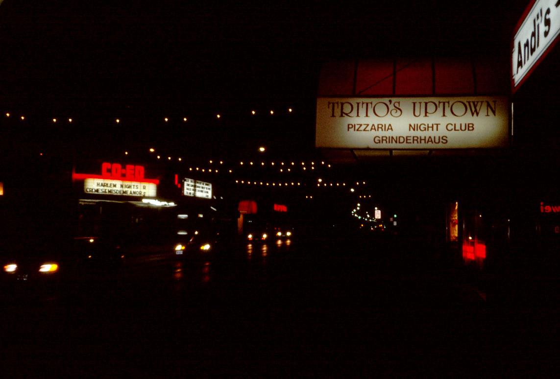 A dark photo of Trito's Uptown's white sign, featuring cars on the street and a Co-Ed Theater marquee across the street