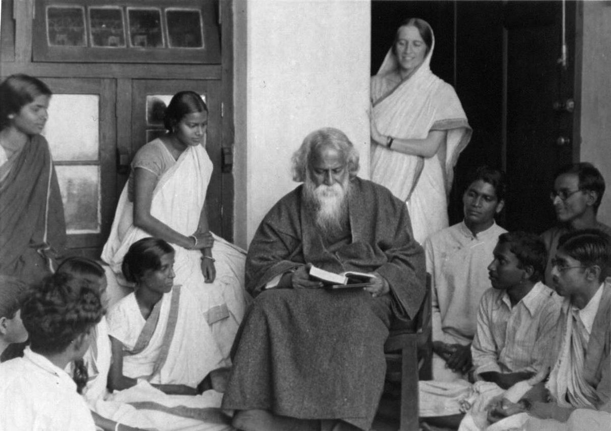 Rabindranath Tagore is seated in a black and white photo surrounded by others listening to him speak