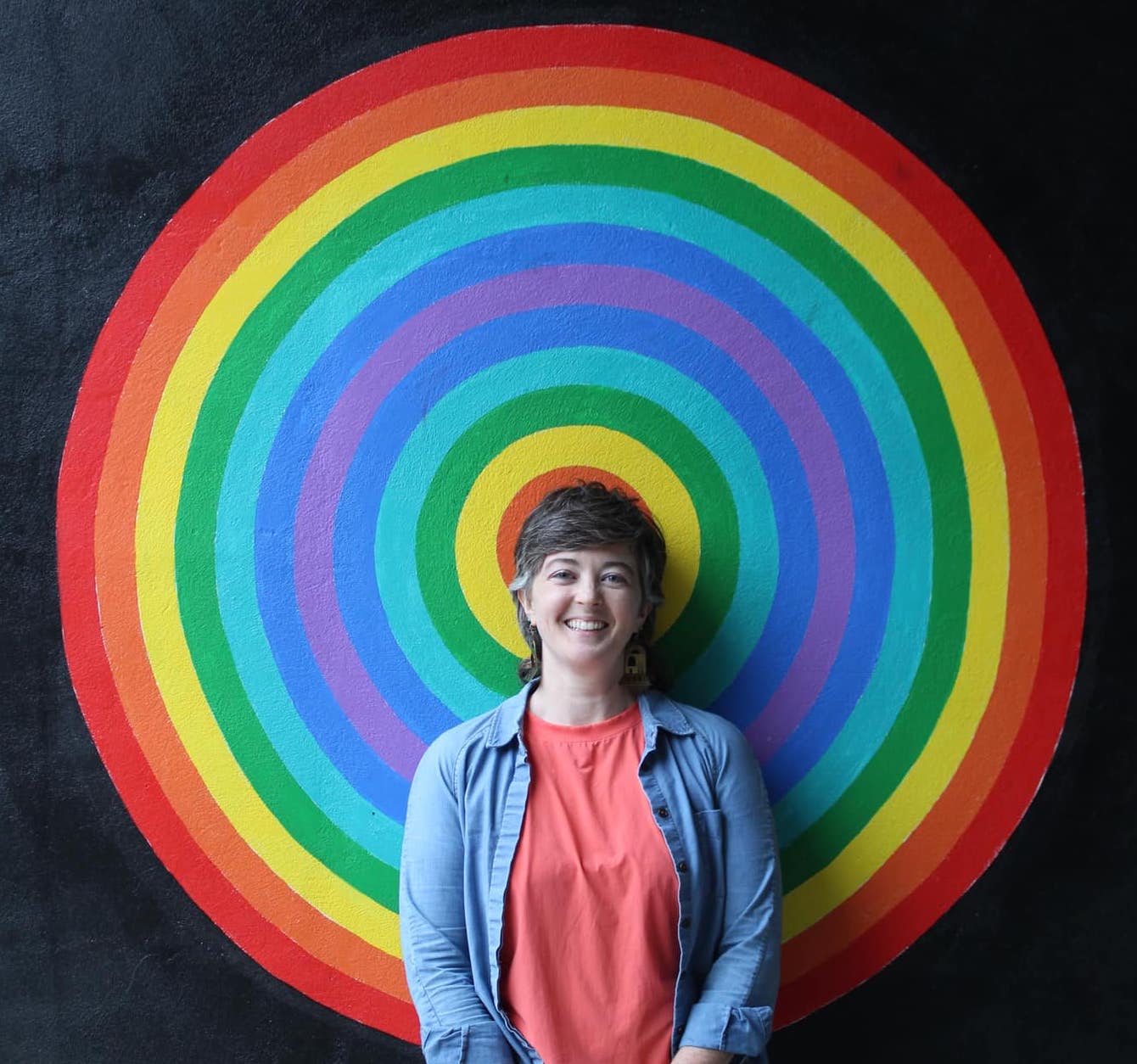 Artist E. Ainsley stands in front of the mural, perfectly centered behind one of the the concentric circles