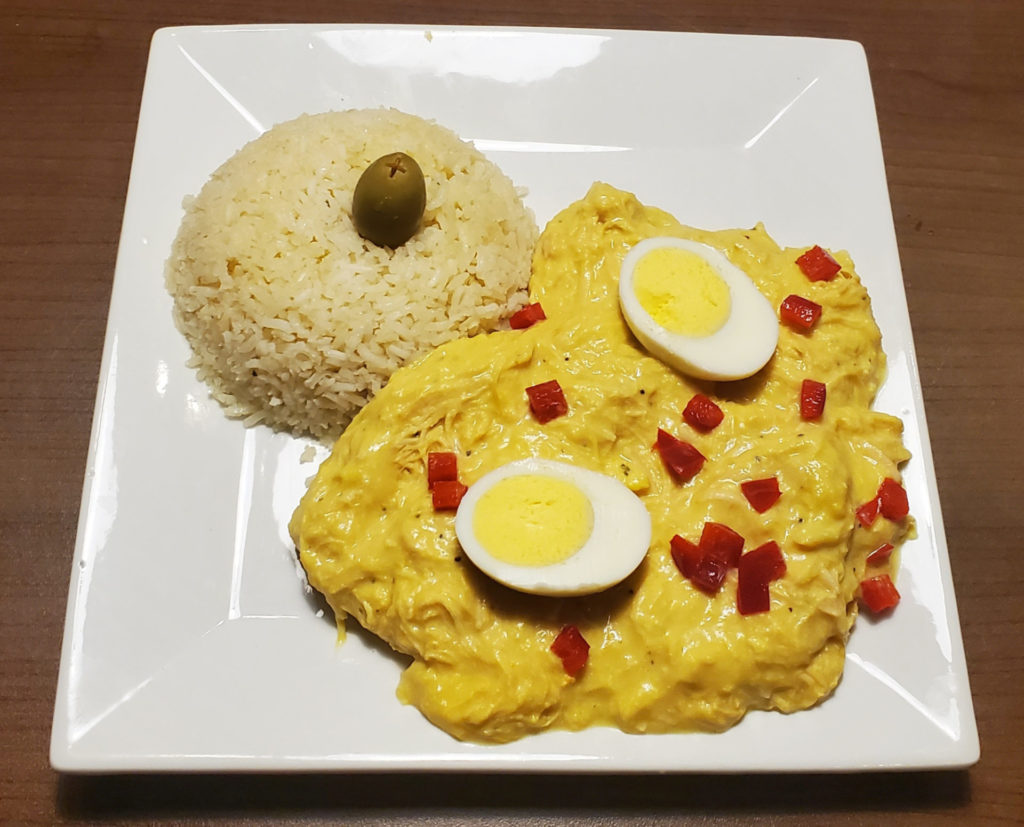 A Peruvian dish of chicken, gravy with hard boiled eggs and a side of rice with an olive on top.