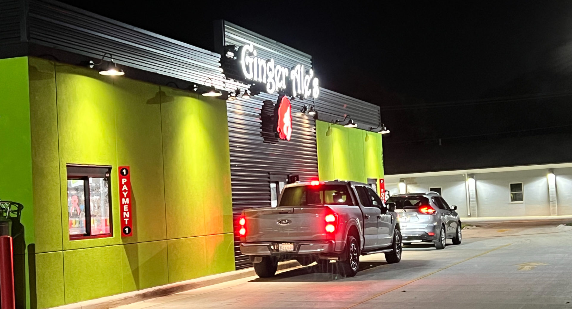 Ginger Ale's of Savoy drive-through at night with two vehicles in line at the lime green building.