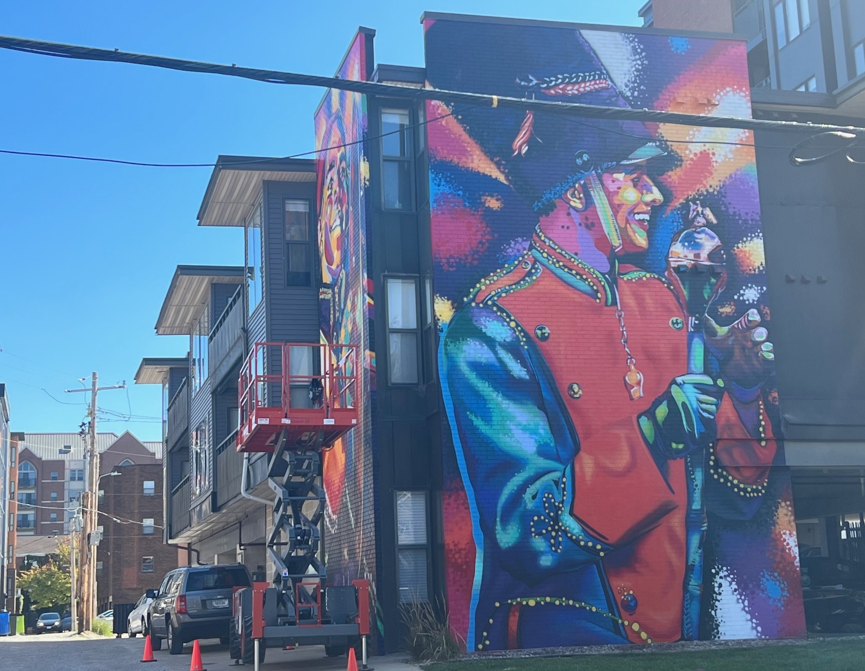 A brightly colored mural depicting a drum major in a marching band uniform stretches from the top to bottom of an apartment building.