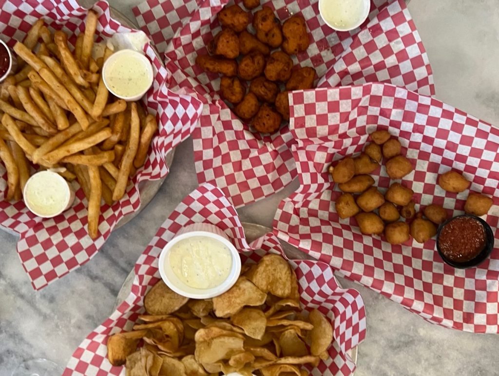 Overhead view of four baskets of appetizers: French fries, house made chips, fried cauliflower, and fried cheese curds.