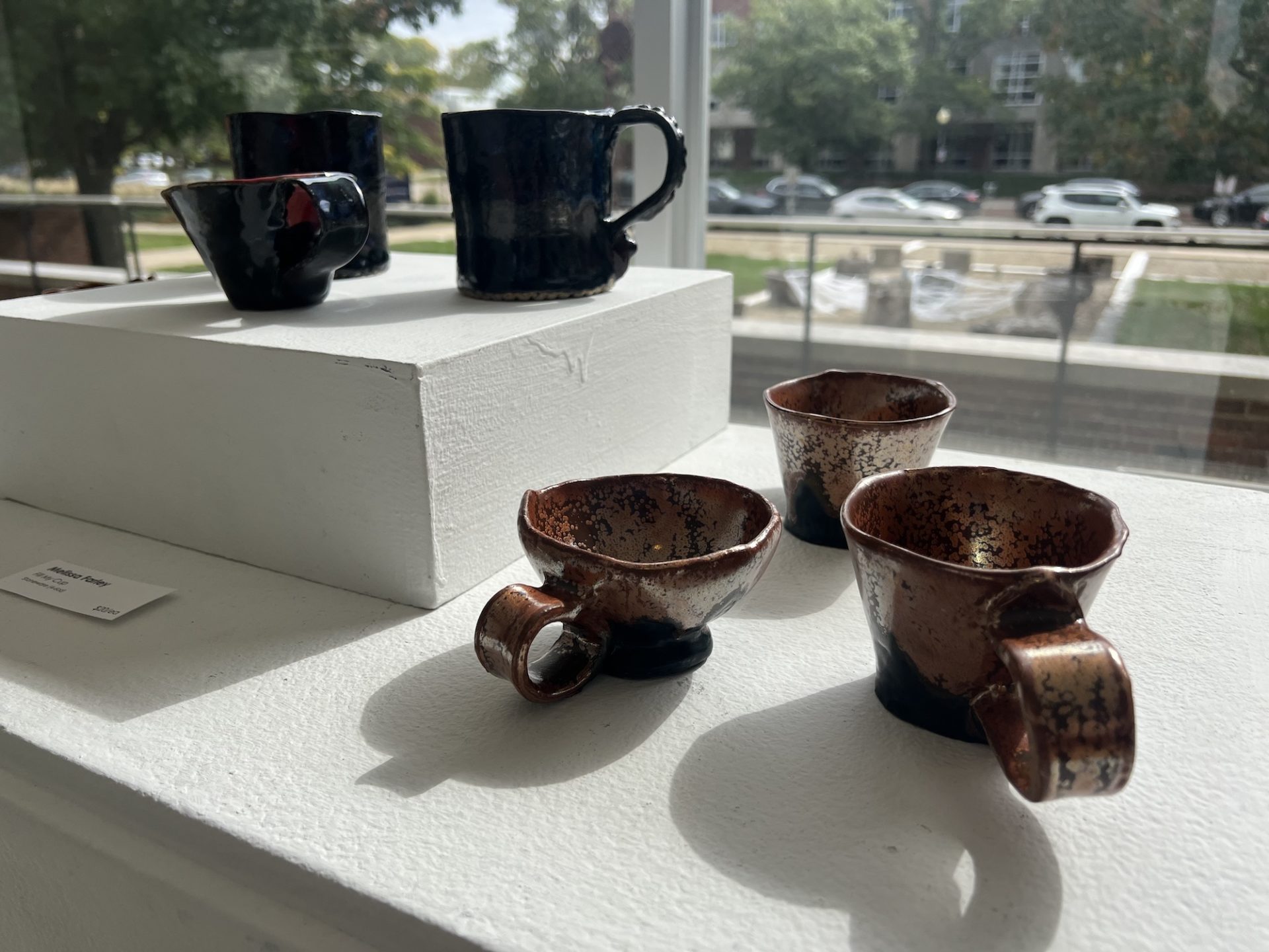 cups sit on a white display in front of a large window