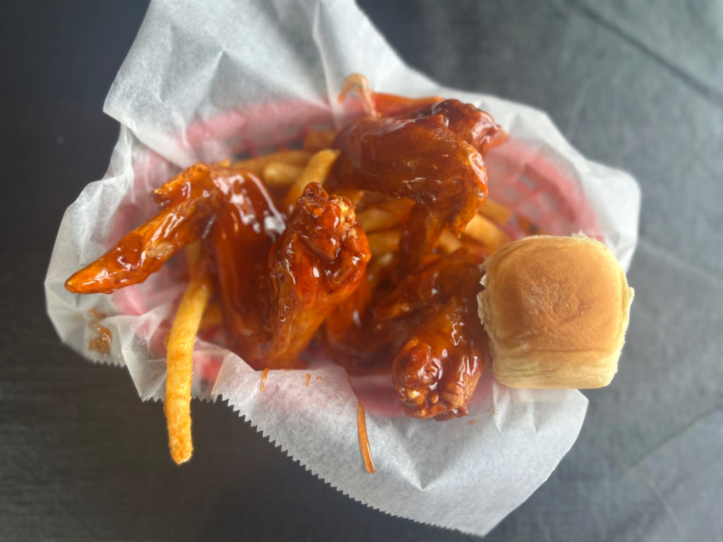 A basket of wings sauced with hot honey, fries, and a dinner roll.