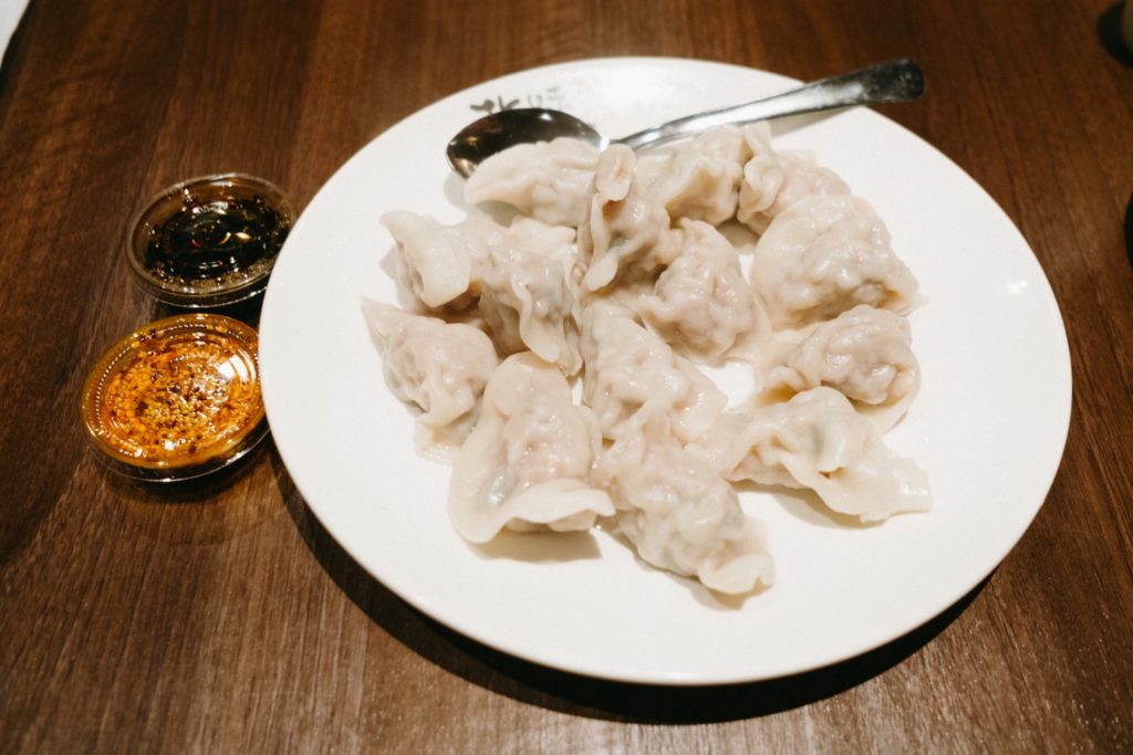 Dumplings on a white plate with silver spoon, two sauces