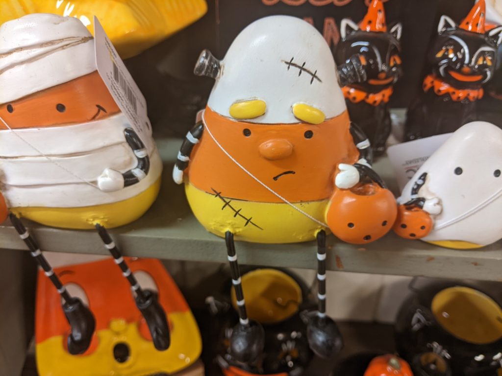 a very sad candy corn figurine with a Frankenstein scar and a tiny pumpkin in it's hands. 