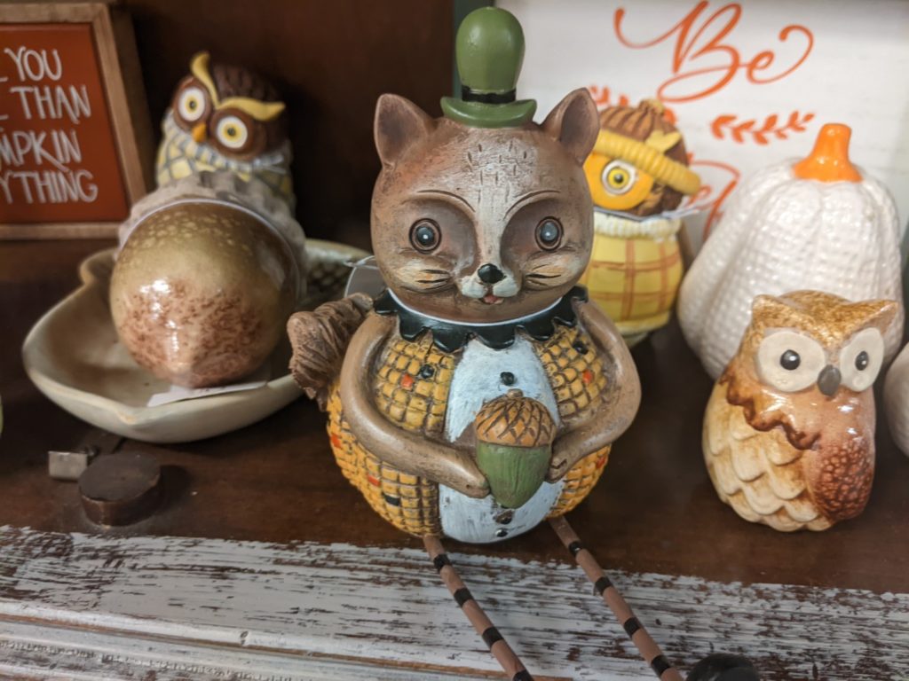 a squirrel figurine dressed up as an ear of corn and sitting on a shelf among other animal figurines