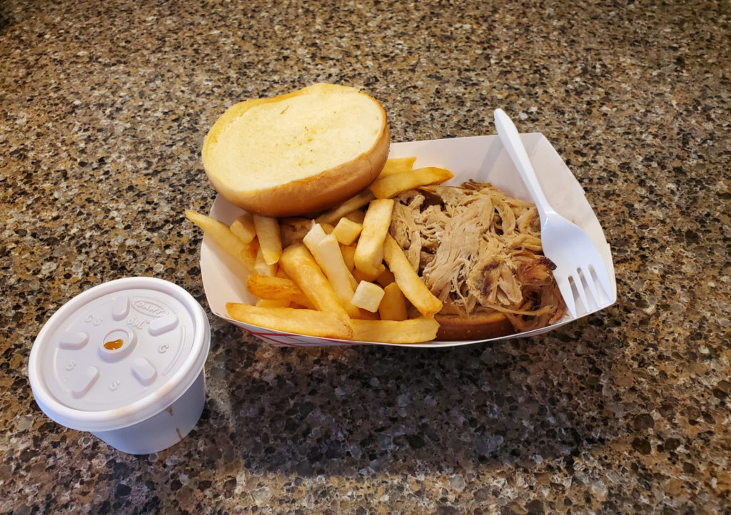 A platter of pulled pork with a bun, plastic fork, and fries.